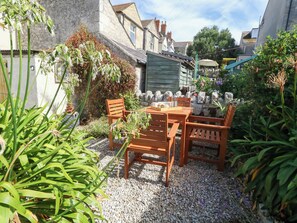 An outdoor patio with a wooden table and chairs, surrounded by gravel and plants. - Quarry Cottage (Portland)
