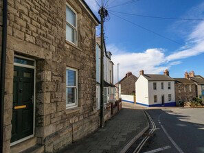 A residential street with stone buildings, a clear sky, and a paved sidewalk. - Quarry Cottage (Portland)
