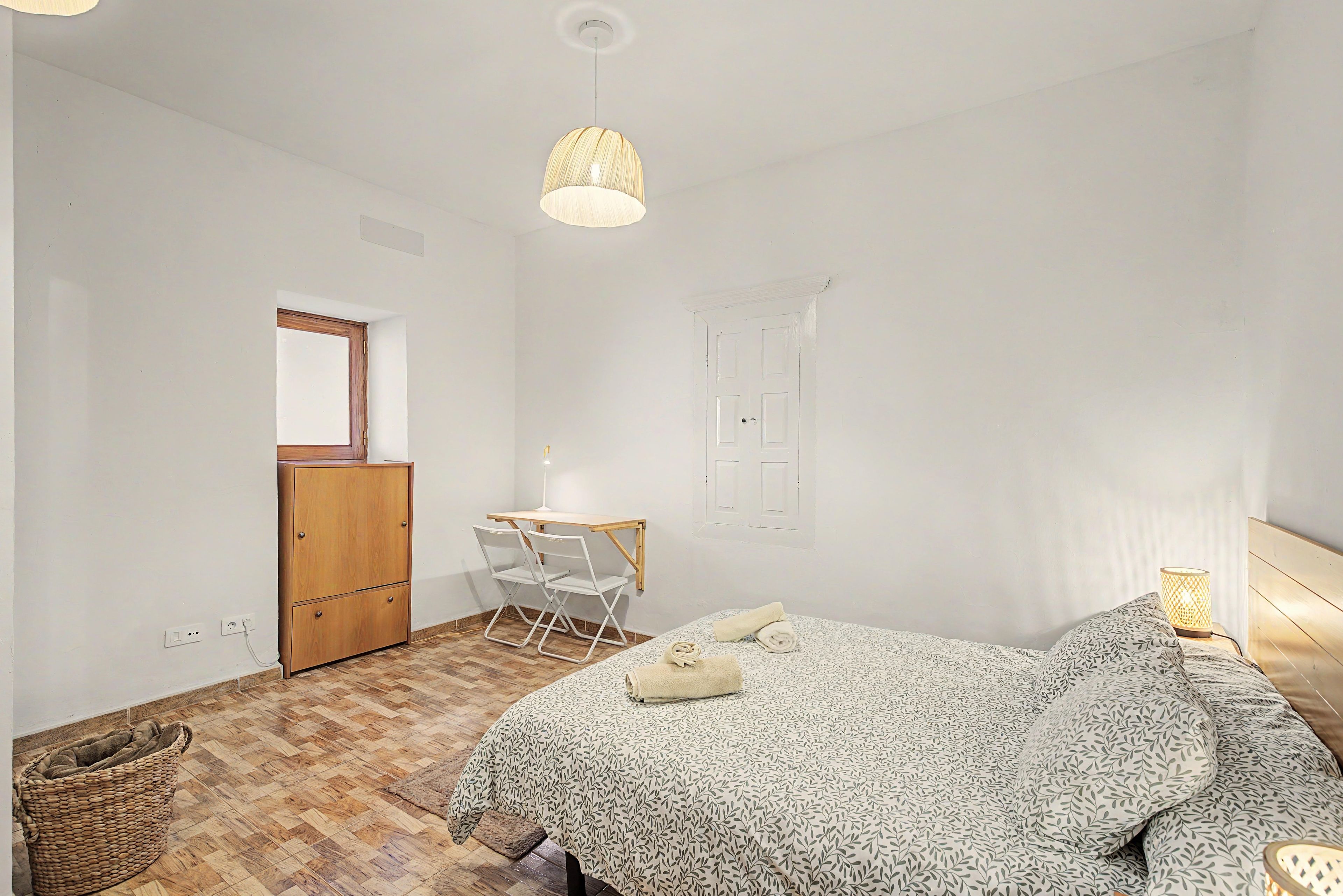 Un dormitorio con una cama, un escritorio con silla, una lámpara colgante y una puerta.