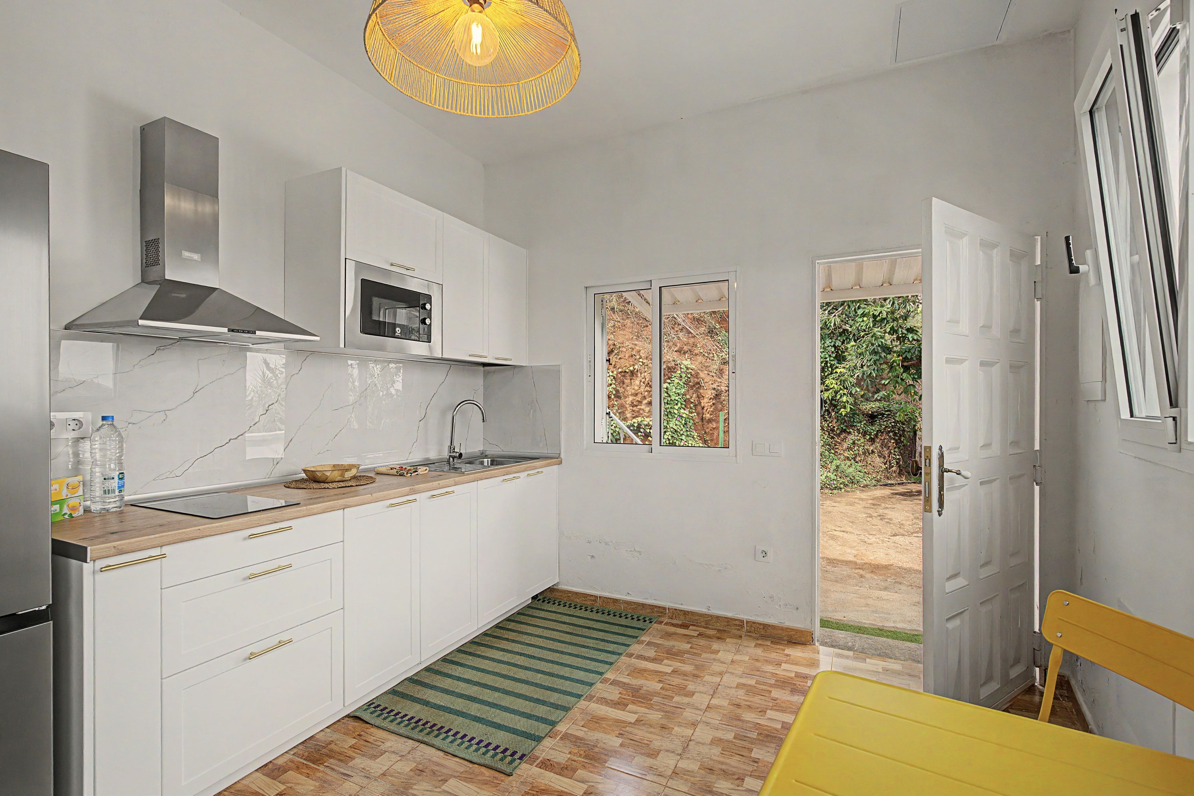 A modern kitchen with white cabinets, a stainless steel range hood, and a microwave.