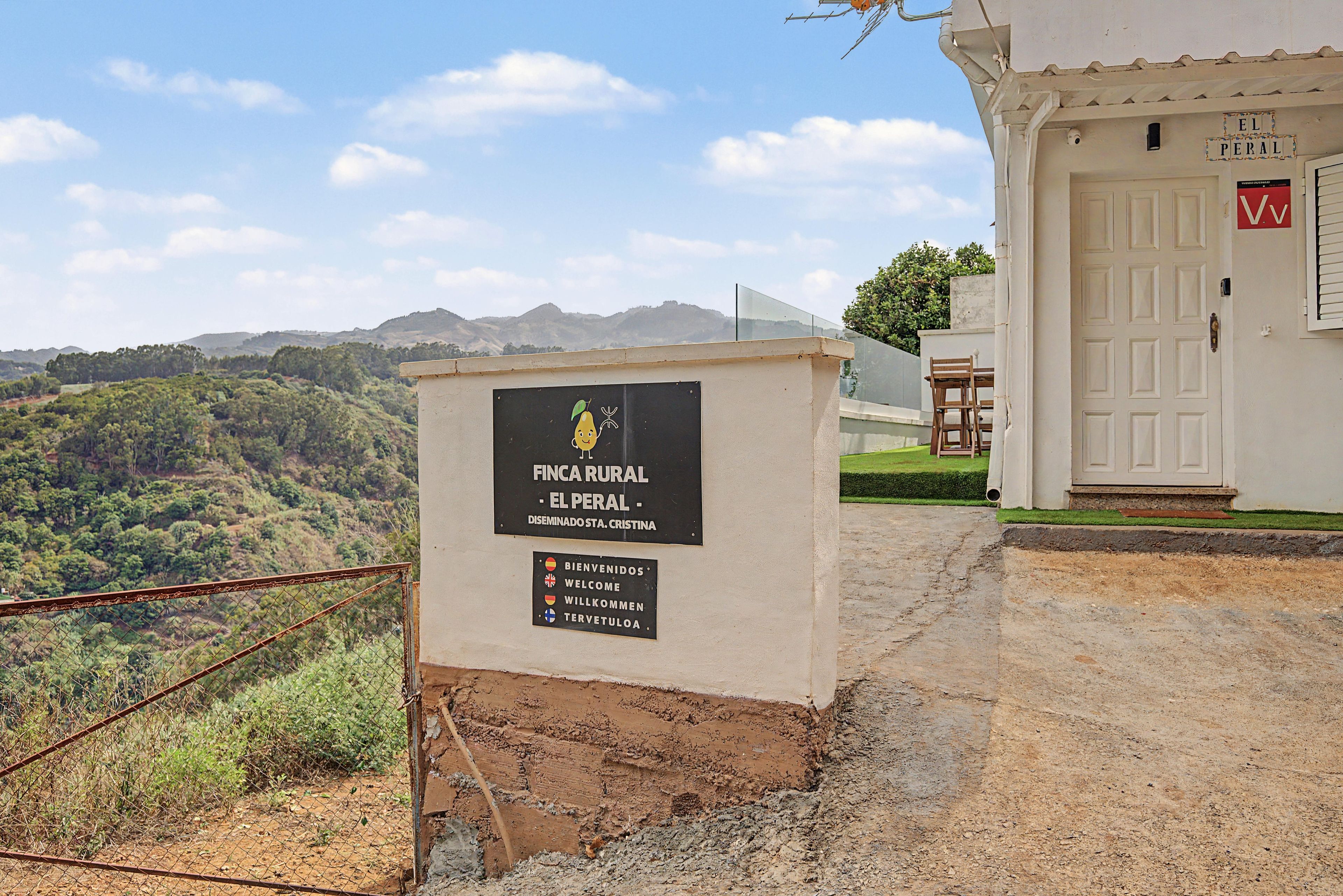 A rural property named 'FINCA RURAL - EL PERAL' with a signboard, a door, and a view of the surrounding landscape.