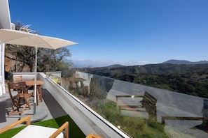 Ein Balkon mit Tisch und Stühlen mit Blick auf eine gebirgige Landschaft.