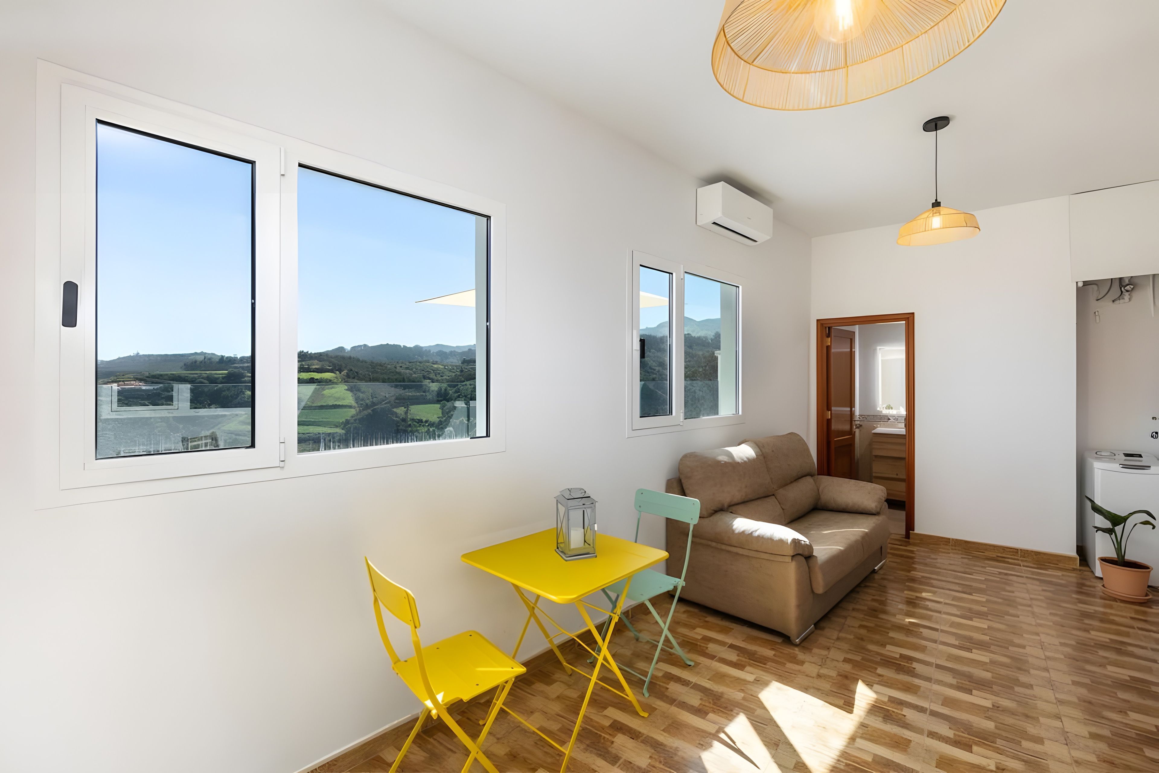 Un salon moderne avec de grandes fenêtres, un canapé, une table jaune et deux chaises.