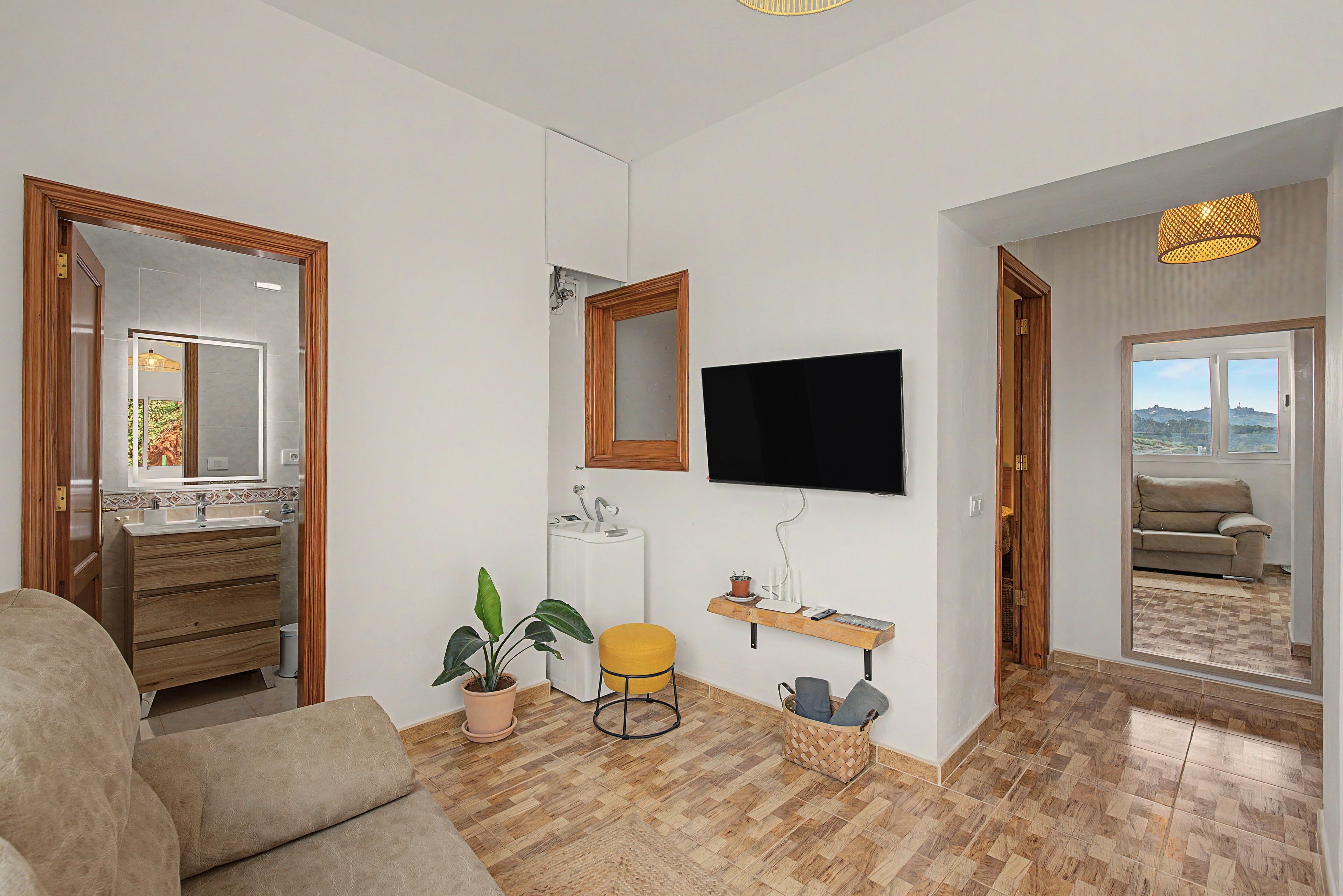 Ein modernes Wohnzimmer mit einer Couch, einem Fernseher, einem Holzkasten, einer Topfpflanze und einem Spiegel.