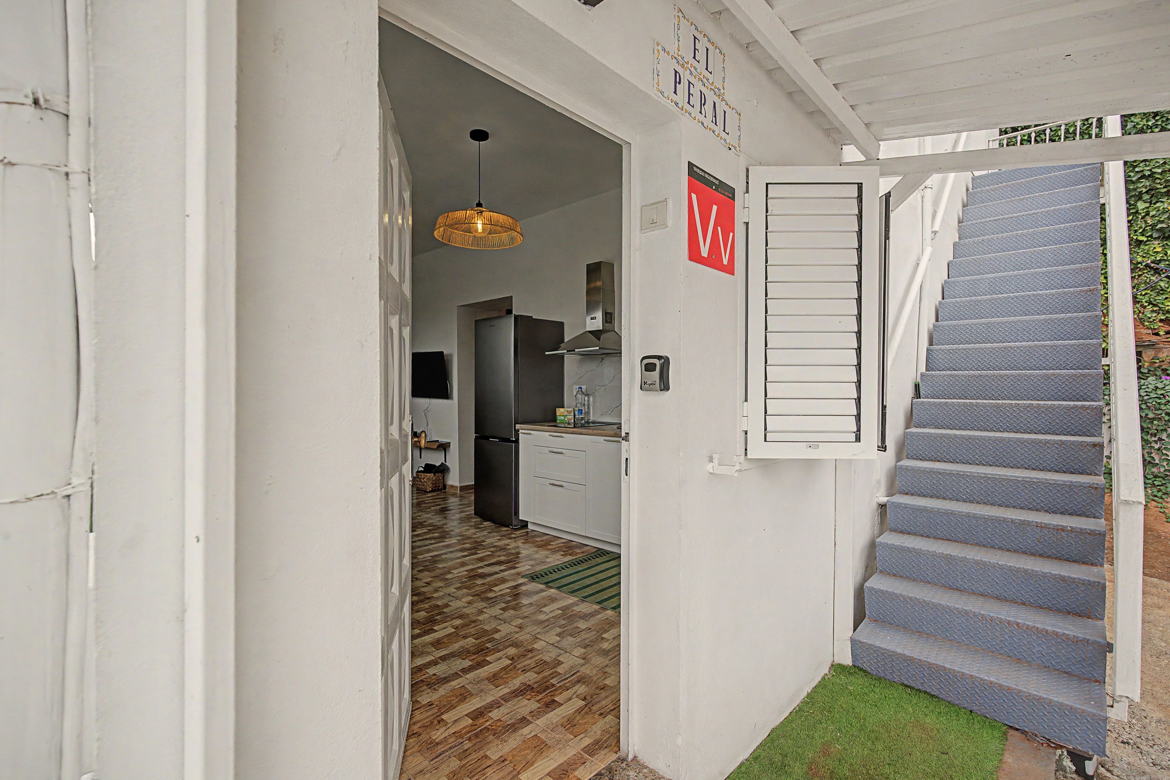 Un couloir étroit avec un escalier menant à un palier, un coin cuisine avec un réfrigérateur et un luminaire suspendu.