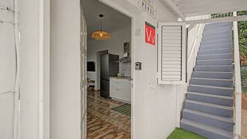 Un couloir étroit avec un escalier menant à un palier, un coin cuisine avec un réfrigérateur et un luminaire suspendu.