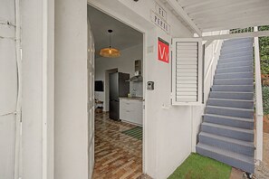 Ein enger Flur mit einer Treppe, die zu einer Zwischenebene führt, einer Küchenzeile mit einem Kühlschrank und einer Hängelampe.