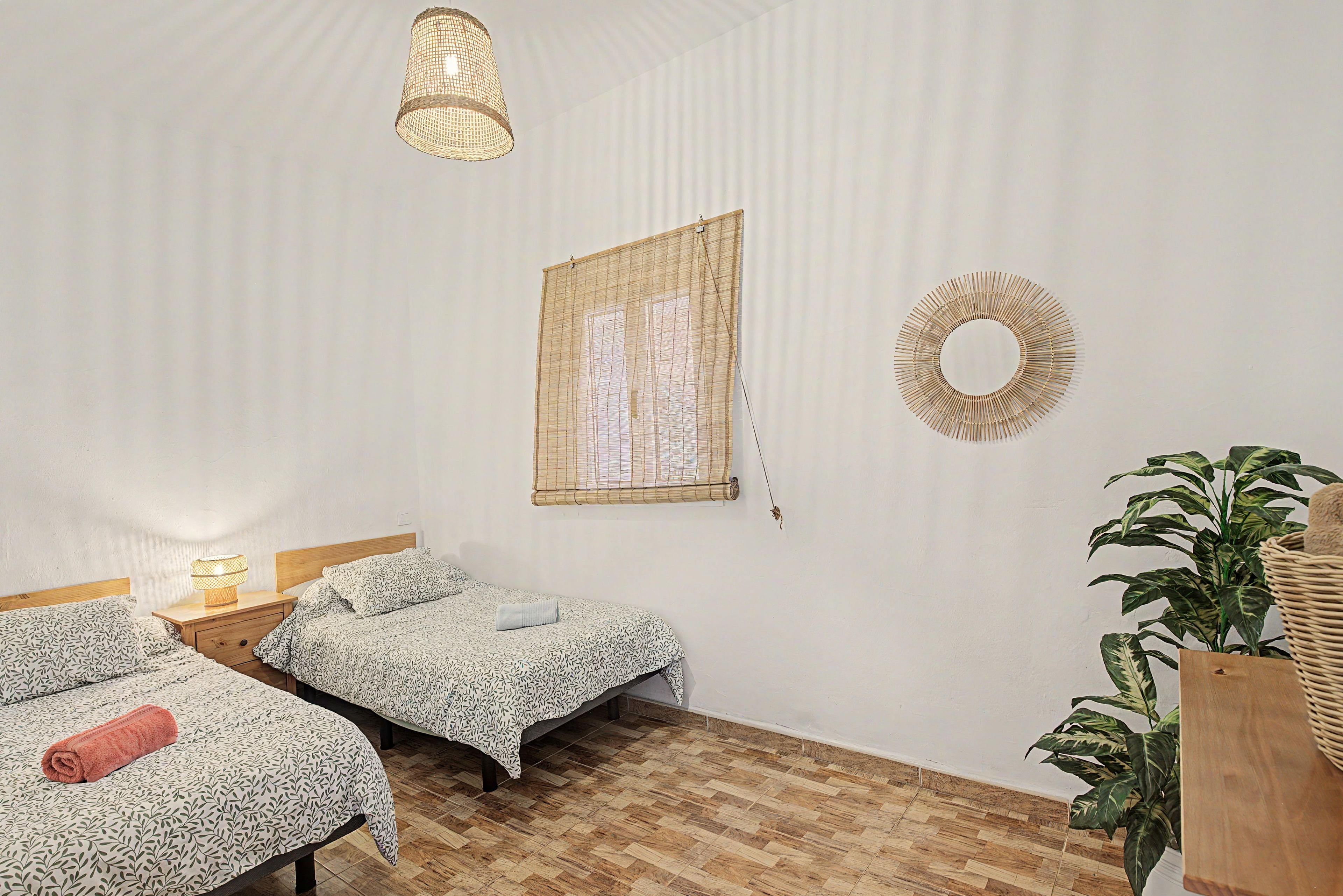 Une chambre avec deux lits simples, un luminaire suspendu, un miroir fixé au mur et une plante en pot.