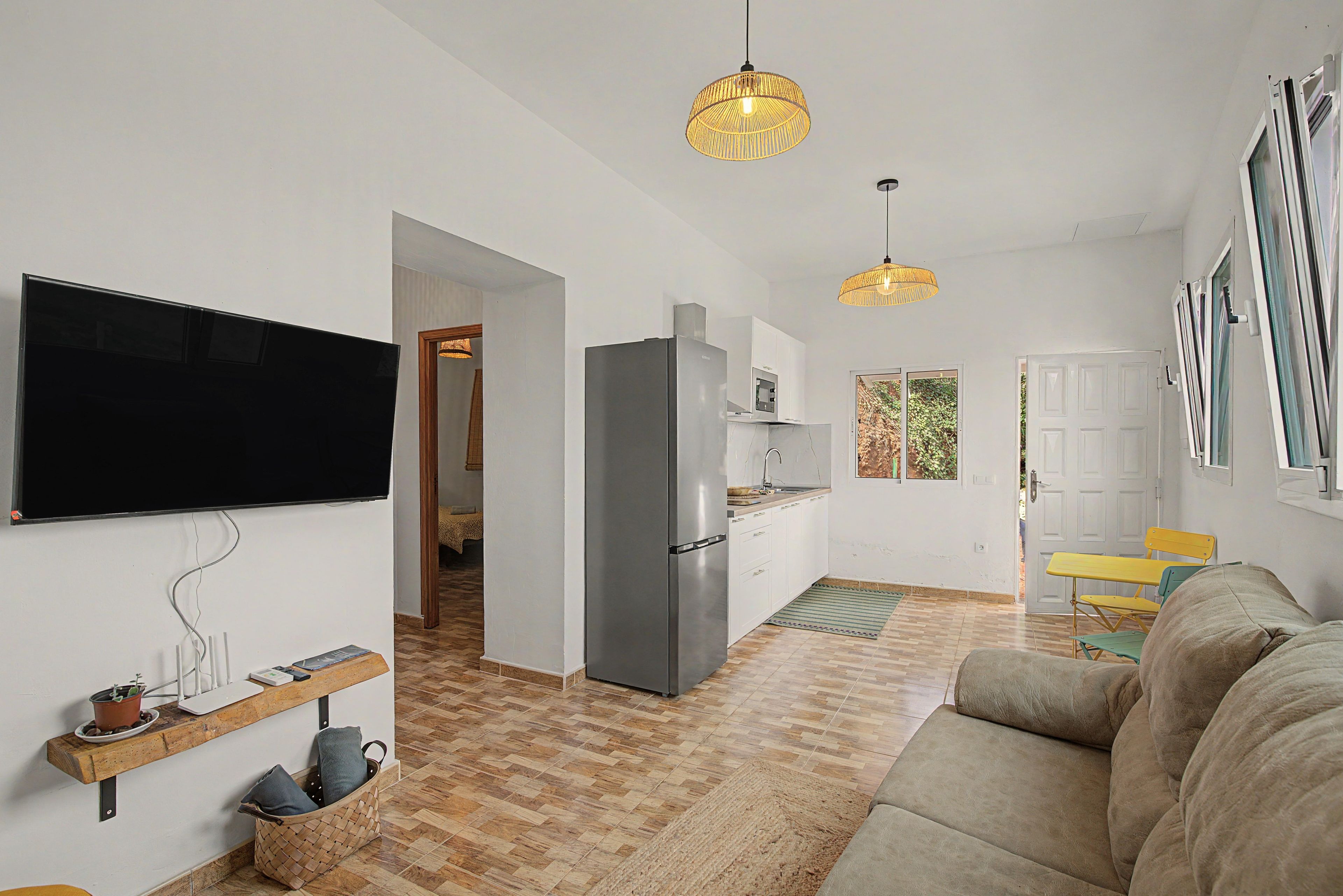 A modern living room with a flat-screen TV, a sofa, and a dining area with a yellow table.
