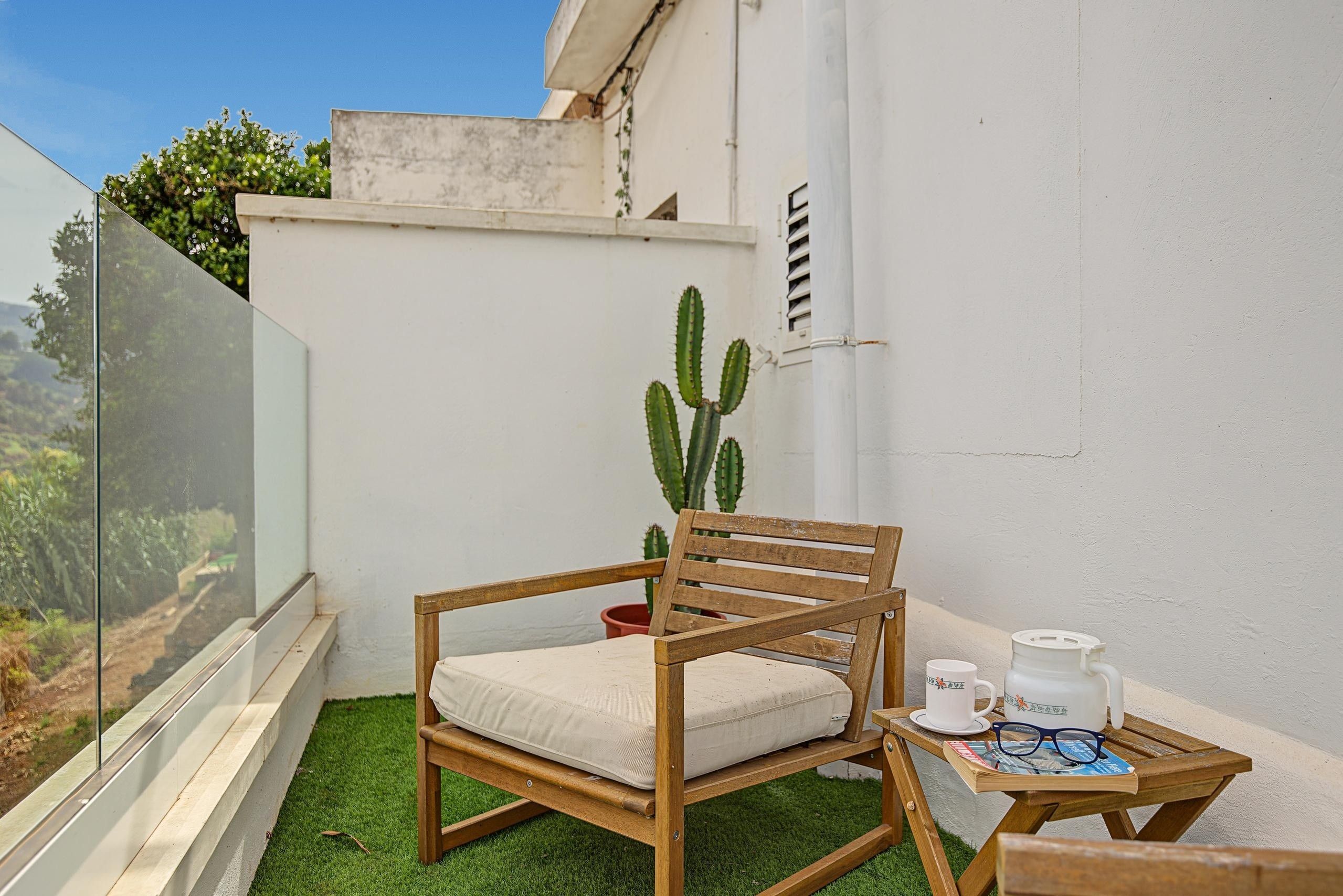 En lille balkon med en træstol, et bord med kop og underkop, og en kaktus som pynt.