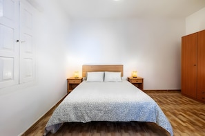 Ein Schlafzimmer mit einem Bett, zwei Nachttischen mit Lampen, einem Holzschrank und einer weißen Wand mit einer Tür.