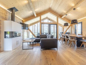 A spacious living area with a high ceiling, wooden beams, a built-in kitchen, and large windows offering a view of the outdoors. - One-bedroom Cabin (Haus)