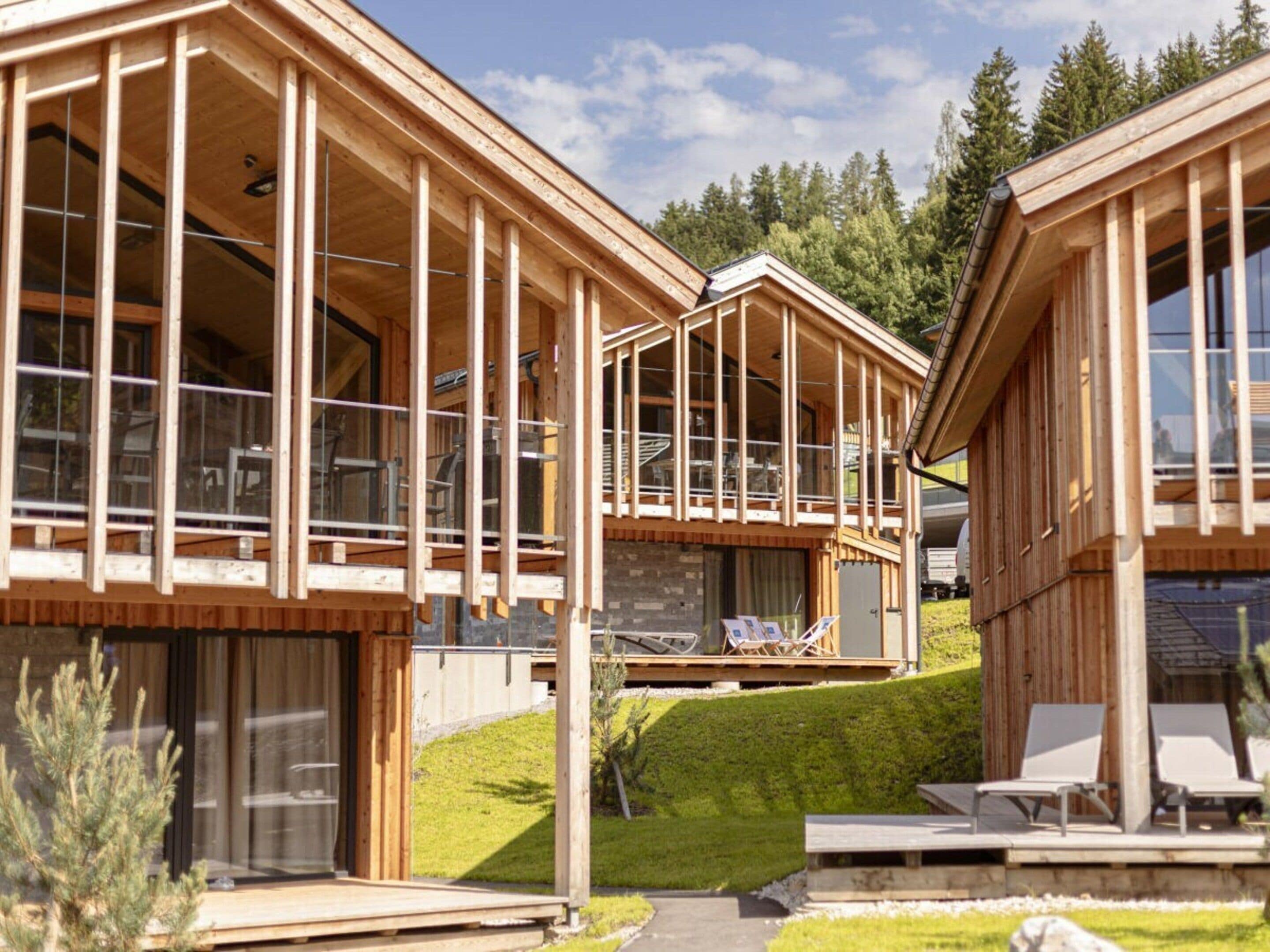 A wooden cabin with large windows, a balcony, and a small deck area.