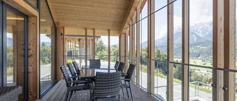 Eine Holzdar Terrasse mit Tisch und Stühlen, große Fenster mit Blick auf die Berge und einem klaren Himmel.