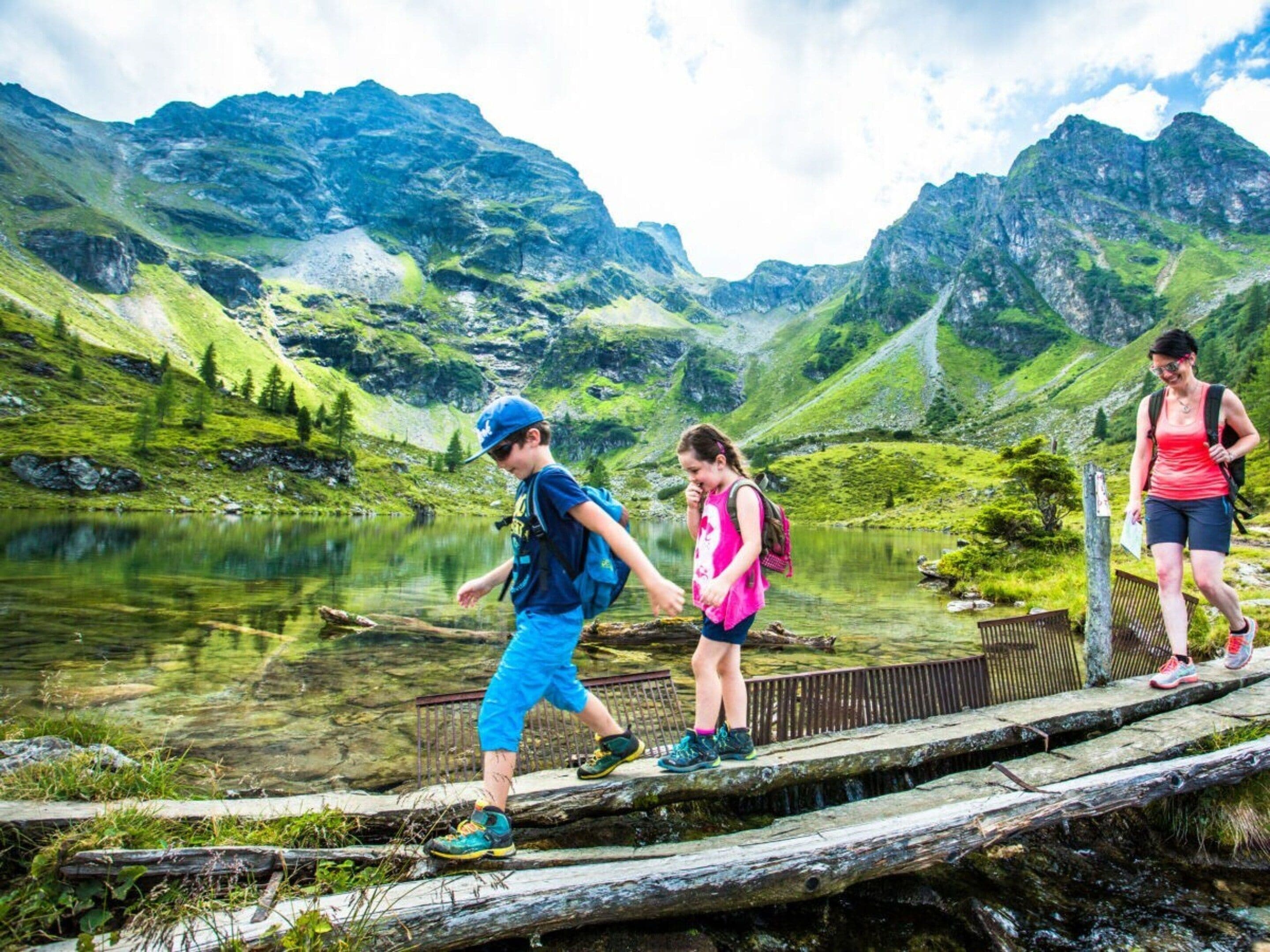 Un grupo de personas caminando sobre un puente de madera cruzando un lago, con montañas al fondo.