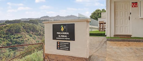 Propiedad rural llamada 'FINCA RURAL - EL PERAL' con un letrero, una puerta y vistas del paisaje circundante.