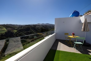 Ein Balkon mit freiem Blick auf eine hügelige Landschaft, einem kleinen Tisch mit Stühlen und einem Blumentopf.