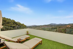 A balcony with a view of a hilly landscape, equipped with two lounge chairs and a small table.