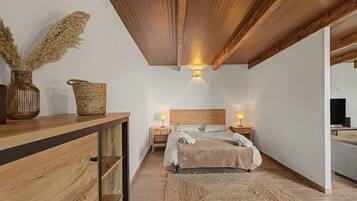 Un dormitorio con techo de madera, una cama con cabecera, mesitas de noche con lámparas, un aparador de madera y una cesta tejida.