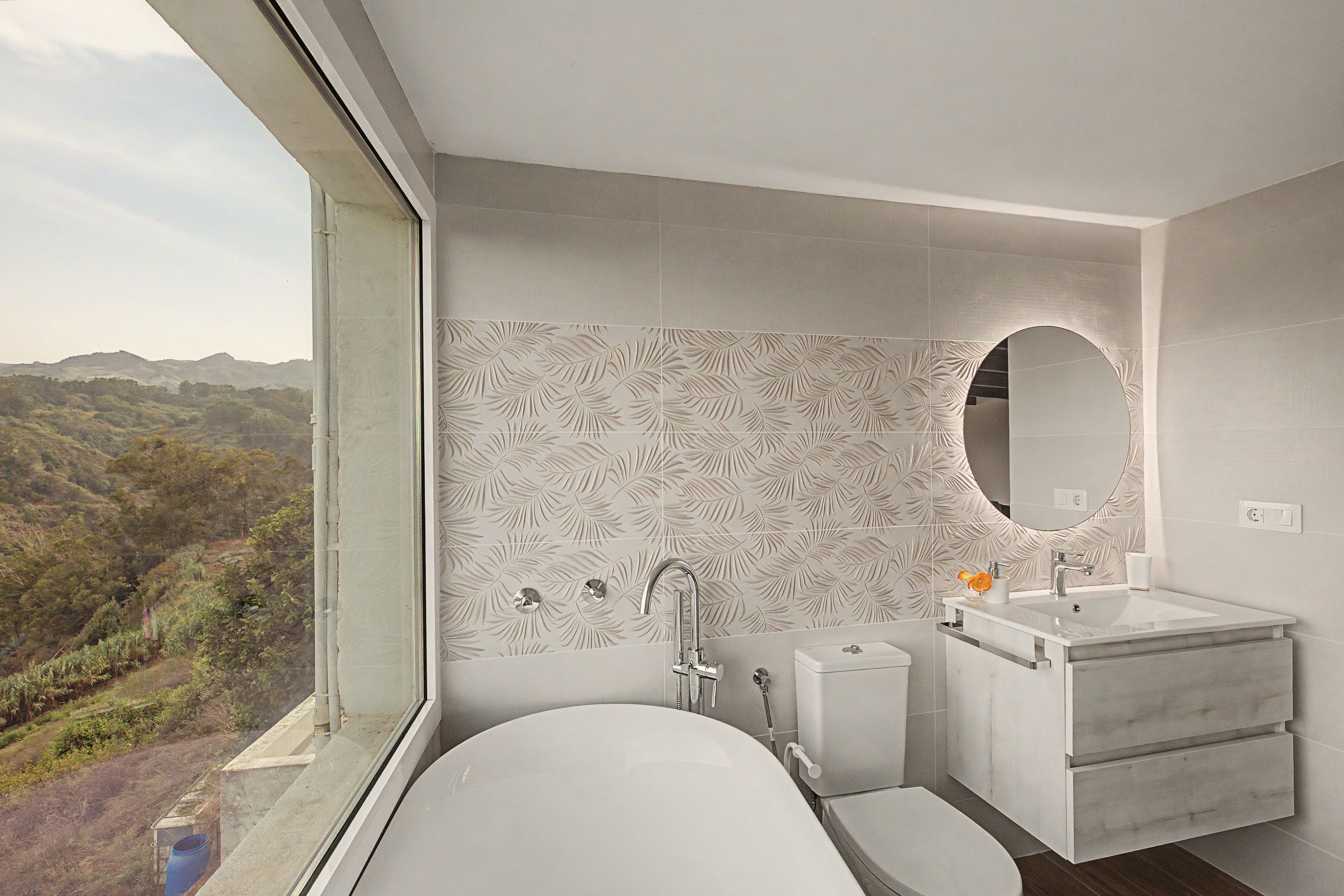 Ein modernes Badezimmer mit Badewanne, Waschbecken und Toilette, ausgestattet mit einem großen Fenster und einer Wand mit dekorativem Blattmuster.