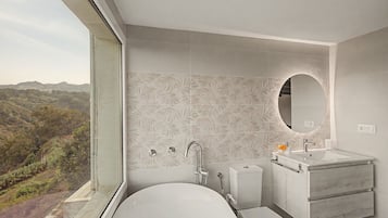 Een moderne badkamer met bad, wastafel en toilet, voorzien van een groot raam en een decoratieve wand met bladmotieven.
