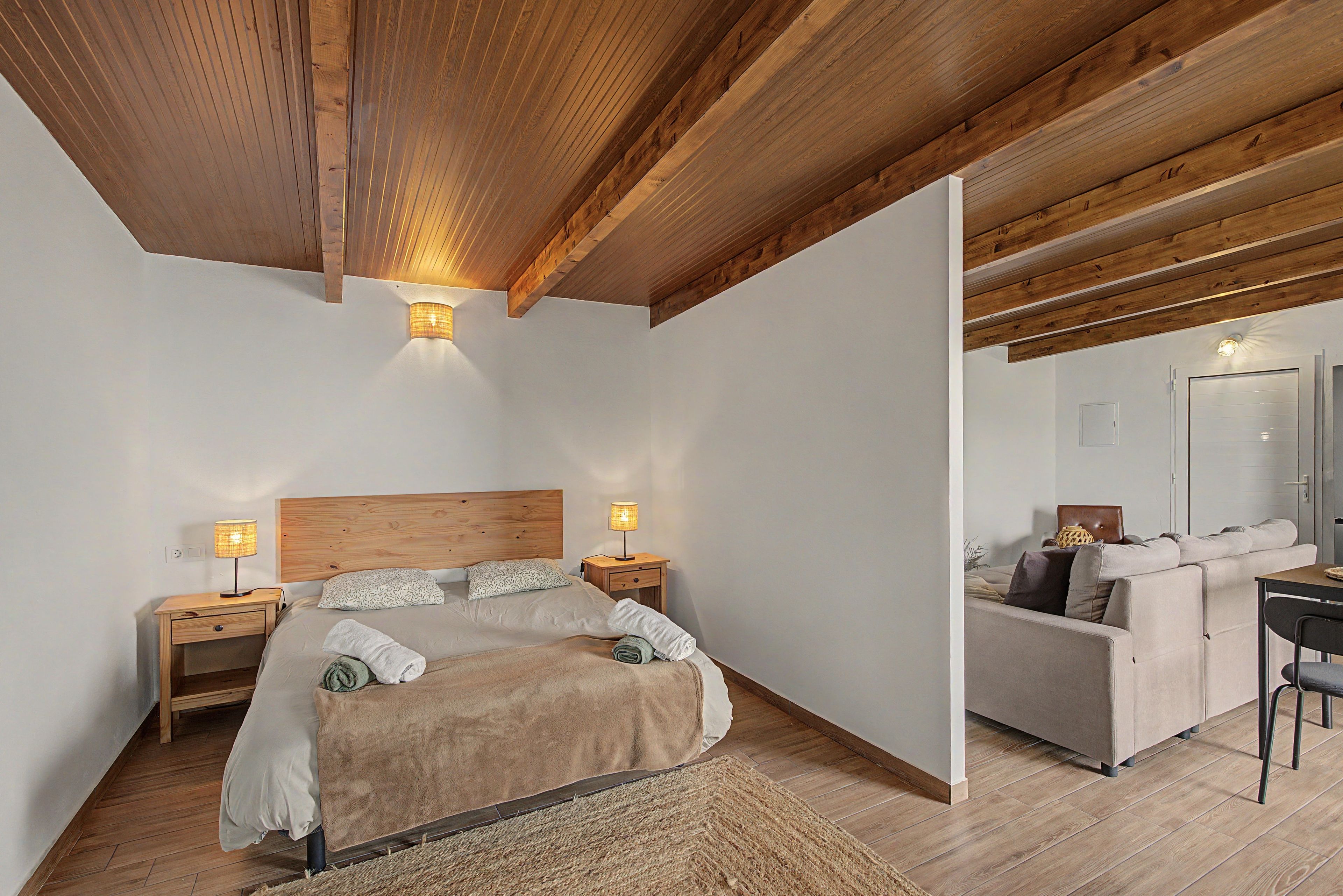 A bedroom with a wooden ceiling, a bed with a headboard, bedside lamps, and a nightstand.