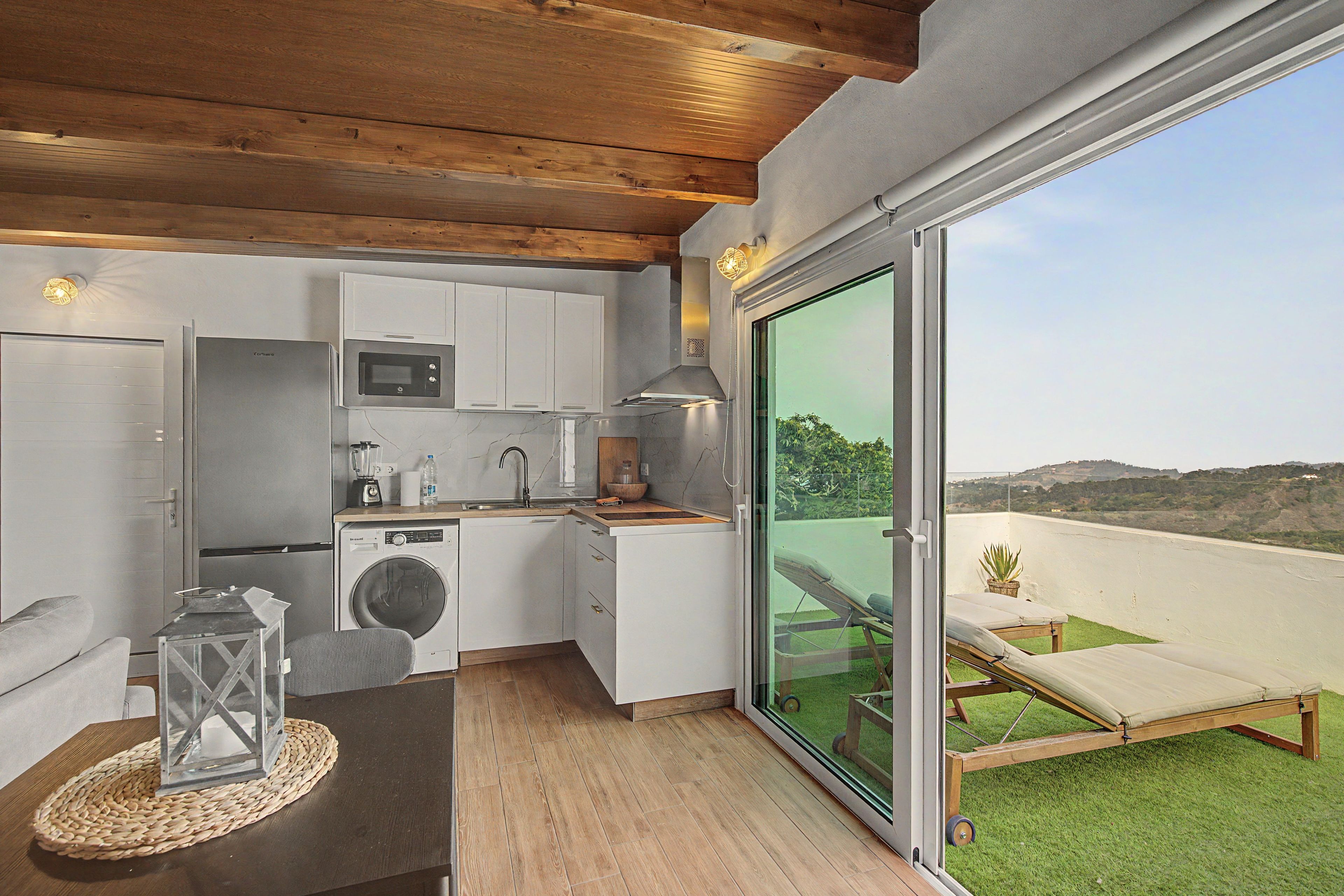 Cocina compacta con electrodomésticos modernos, comedor con mesa y silla, y balcón con vistas.
