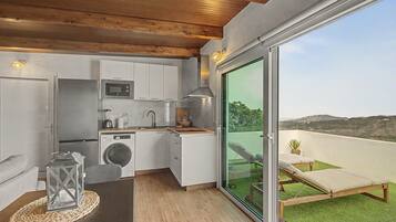 Cocina compacta con electrodomésticos modernos, comedor con mesa y silla, y balcón con vistas.
