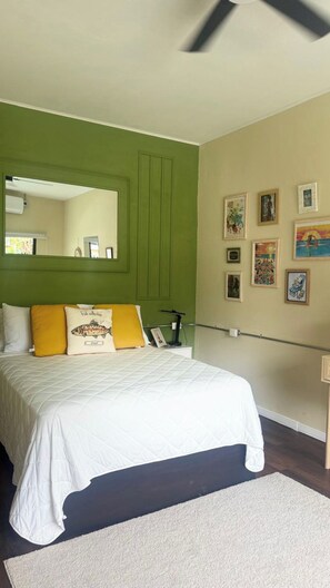 Ein Schlafzimmer mit einem Bett, grünen Wänden, einem Deckenventilator und gerahmten Bildern an der Wand.