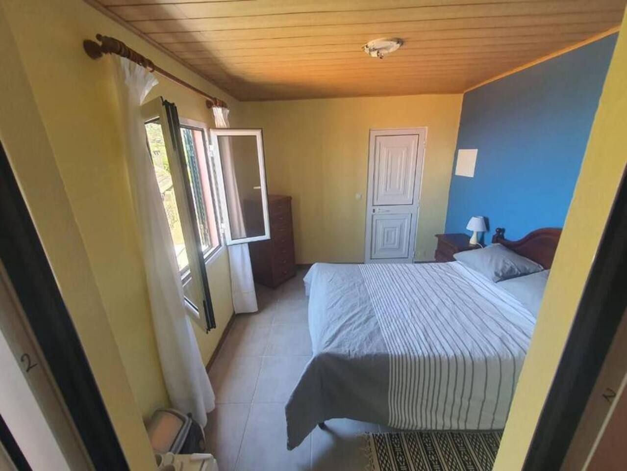 Ein Schlafzimmer mit Bett, Nachttisch, Kommode und einem Fenster mit Vorhängen.