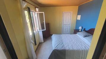 Ein Schlafzimmer mit Bett, Nachttisch, Kommode und einem Fenster mit Vorhängen.