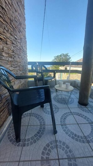 Zona de pati amb mur de pedra, una cadira de plàstic negre, taula petita rodona amb dues tasses blanques i un pal metàl·lic.