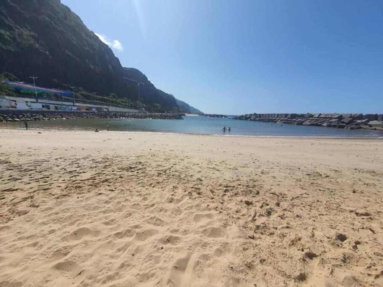 A sandy beach with a rocky shoreline and a mountain in the background.