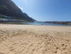 A sandy beach with a rocky shoreline and a mountain in the background. - Private room with en-suite and private access (Calheta)