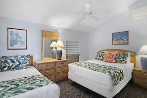 A hotel room with two beds, a ceiling fan, a nightstand with a lamp, a dresser, and artwork on the walls.