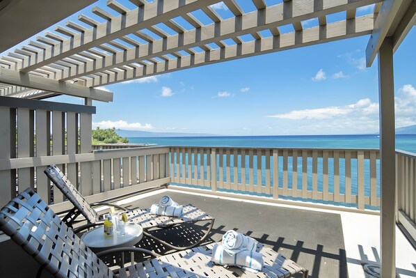 A balcony with a view of the ocean, lounge chairs, and a small table with a bottle and glass.