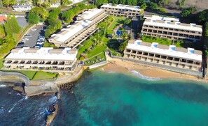 A coastal hotel with multiple buildings, a beach, and a parking area.