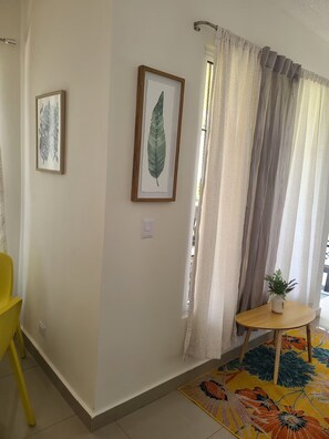 A room with a yellow chair, a small round table with a plant, and two framed leaf artworks on the wall.