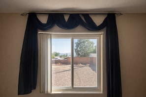 A room with a large window, a view of a gravel area, and a brick wall. - Escape to Tangled Desert Nest- 3B/2B where your lake days & desert sunsets meet! (Lake Havasu City)