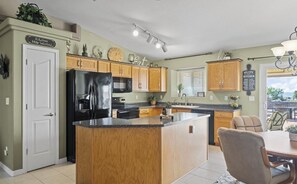 A kitchen with a central island, wooden cabinets, a black refrigerator, and a dining area with chairs. - Escape to Tangled Desert Nest- 3B/2B where your lake days & desert sunsets meet! (Lake Havasu City)