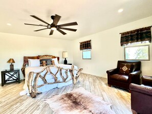 A bedroom with a bed, a ceiling fan, a window with curtains, a leather armchair, and a rug. - Bear Down Arizona- It's Gametime! (Tucson)