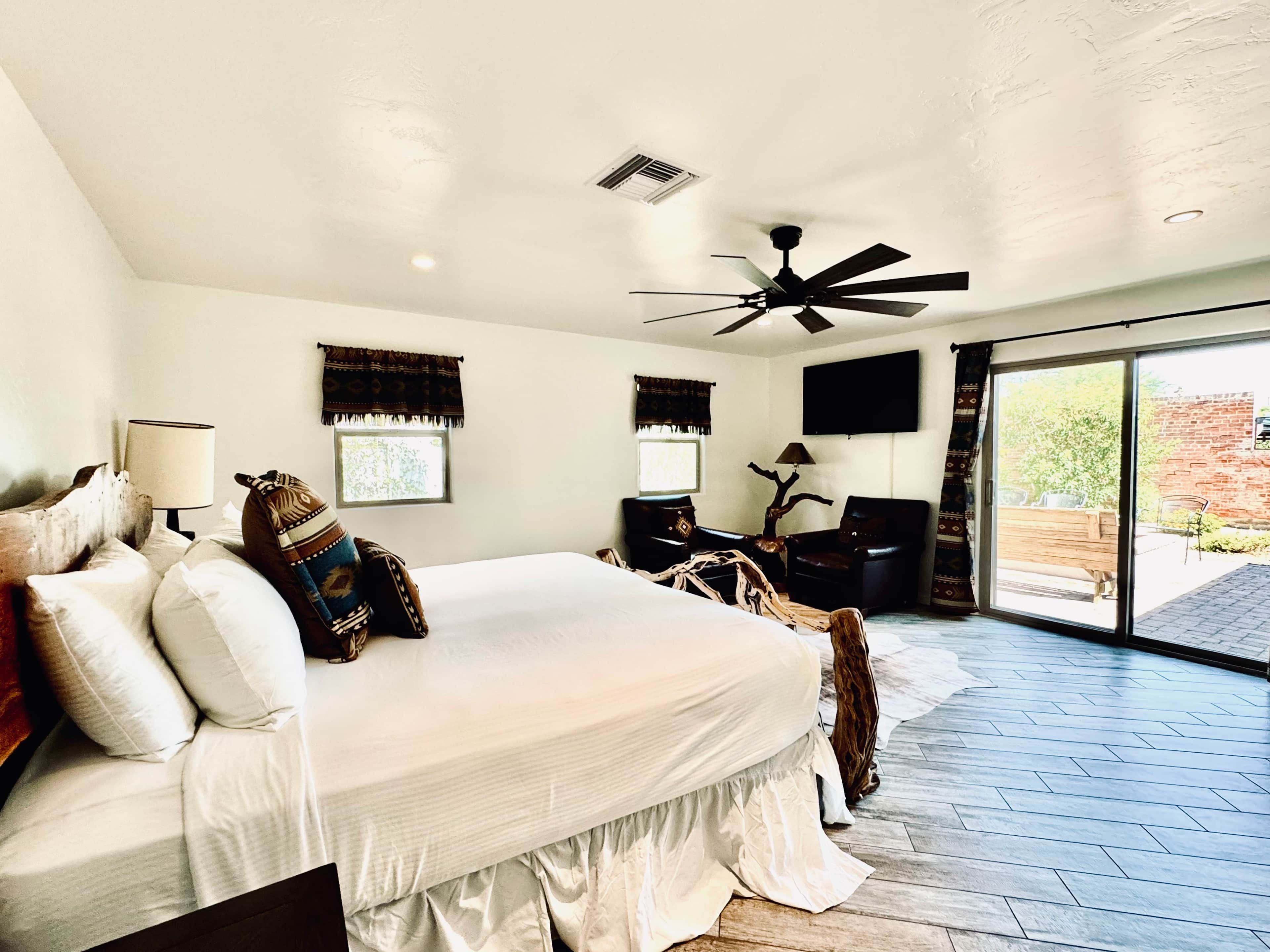 A bedroom with a large bed, a ceiling fan, a television, and a sliding glass door to the outside.