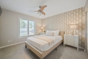 Ein Schlafzimmer mit einem Bett, einem Deckenventilator, einem Fenster und einer Wand mit Muster.
