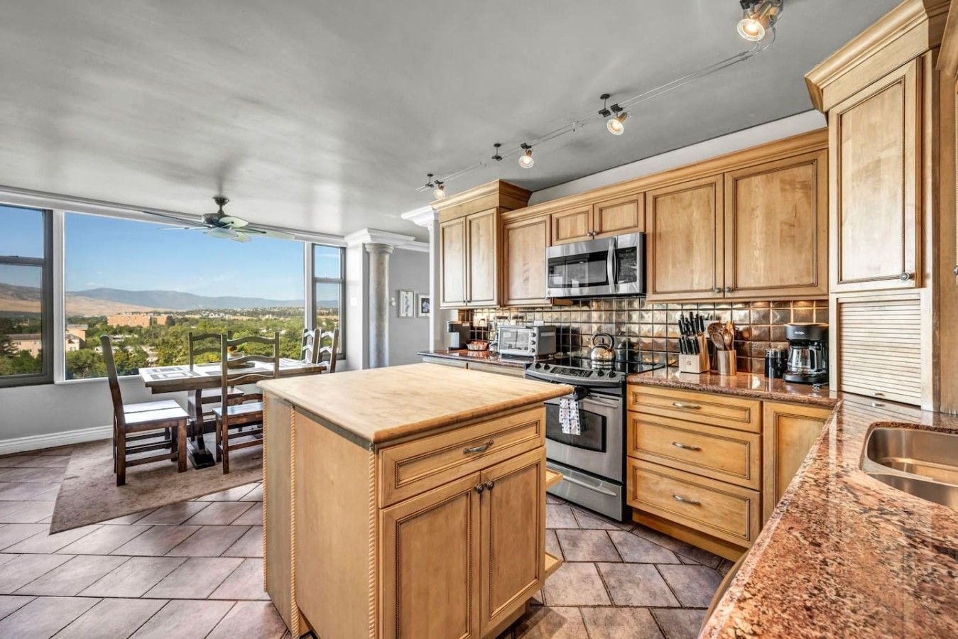 A kitchen with wooden cabinets, a large island, stainless steel appliances, and a view of the landscape.