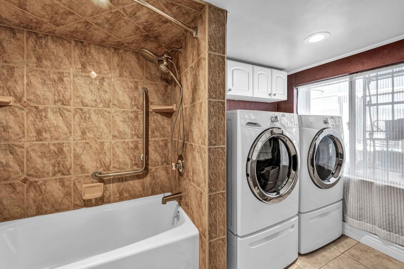 A bathroom with a bathtub, a shower with a handheld showerhead, and a front-loading washing machine.