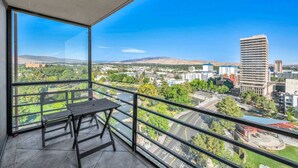 A balcony with a table and chairs, overlooking a cityscape with buildings and a river. - Reno Penthouse | Private Balcony | Mountain Views (Reno)