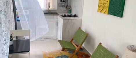 Un espace de vie compact comprenant un coin cuisine, un ventilateur de plafond, un tapis à motifs et une petite table avec une lampe.