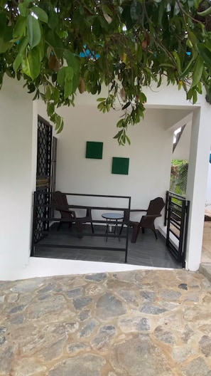 A covered outdoor seating area with a table and chairs, a stone floor, and a gate.