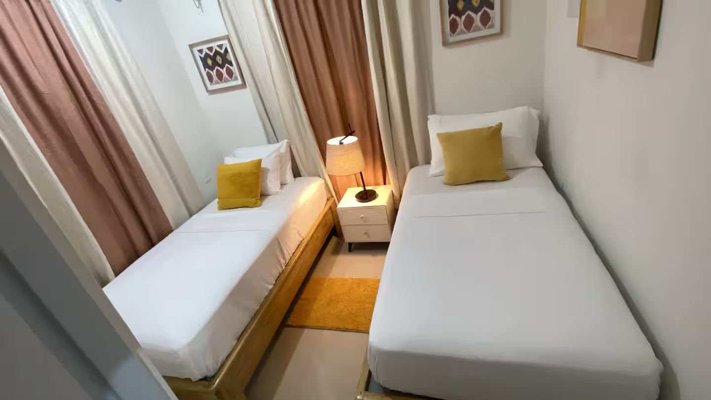 Une chambre d’hôtel avec deux lits simples, une table de chevet, une lampe et une petite table.