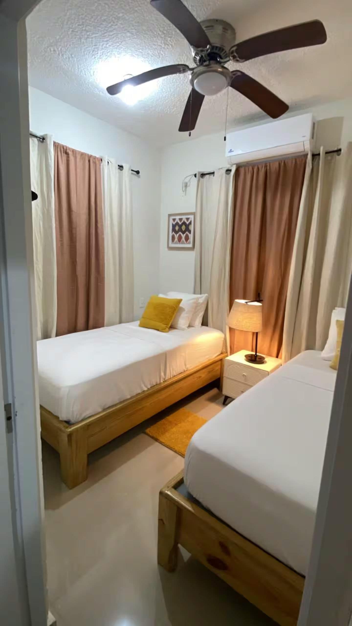 A bedroom with two beds, a ceiling fan, and a nightstand with a lamp.